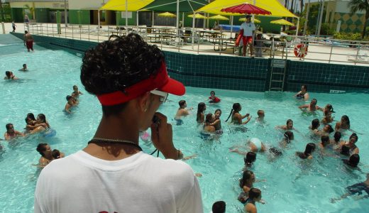 Lifeguard in a white lifeguard shirt and red visor watching swimmers in a busy outdoor pool